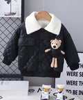 Black quilted jacket with white fur collar and teddy bear toy on a hanger against a gray wall.