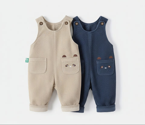 Two children's overalls, one beige and one blue, hanging on wooden hangers against a white background.