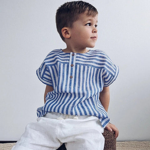 Child wearing a blue and white striped shirt sitting on a woven stool against a plain background