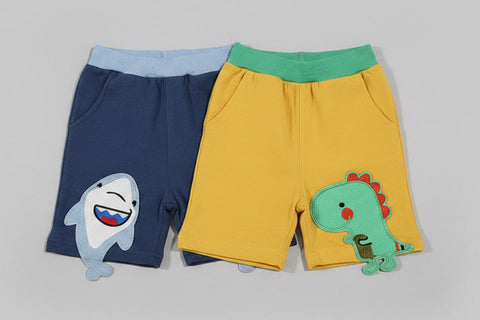 Two pairs of children's shorts with animal designs on a gray background, accompanied by a toy airplane and life buoy.