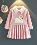 Pink children's dress with swan design on a hanger against a dark background