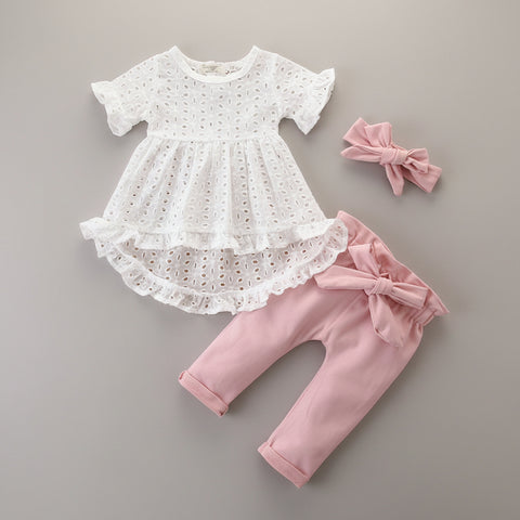 White lace dress and pink pants with a bow on a wooden surface.