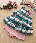 Children's dress with cherry pattern and pink shorts on a wooden surface.