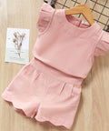 Pink children's outfit with ruffled top and shorts on a wooden surface.