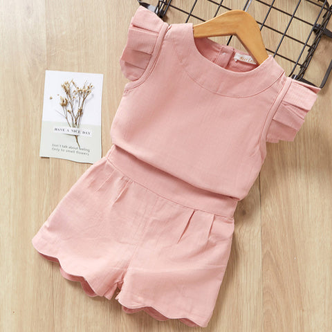 Pink children's outfit with ruffled top and shorts on a wooden surface.