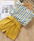Yellow shorts and patterned top on a wooden surface with a magazine in the background