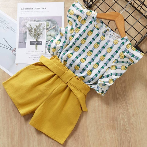 Yellow shorts and patterned top on a wooden surface with a magazine in the background