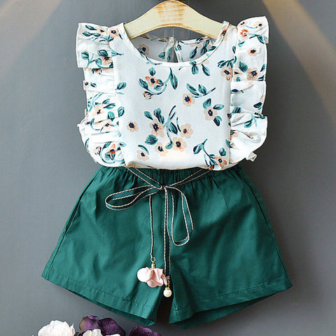 Children's outfit with floral top and green shorts on a gray background