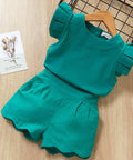 Green children's outfit with ruffled details on a wooden surface