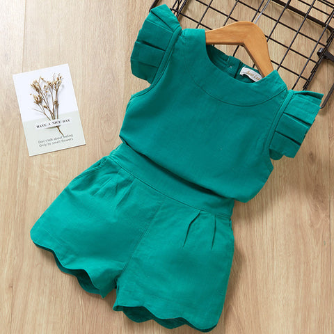 Green children's outfit with ruffled details on a wooden surface