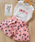 White sleeveless top with a pink skirt featuring bird patterns on a wooden surface.
