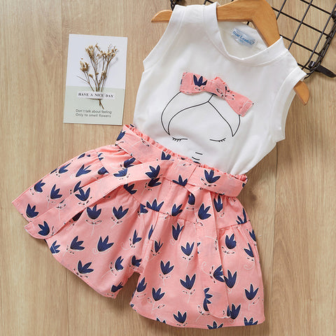 White sleeveless top with a pink skirt featuring bird patterns on a wooden surface.