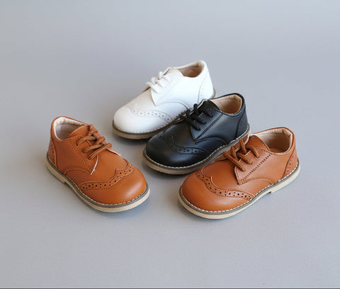 Set of children's shoes including brown, black, and white pairs on a textured surface.
