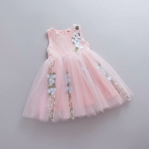 Pink floral dress on a gray surface with a basket and leaf decoration in the background.