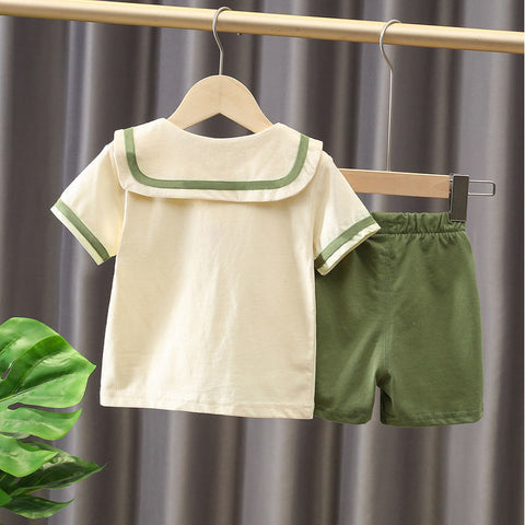 Children's outfit with white shirt and green shorts on a hanger against a gray curtain background.