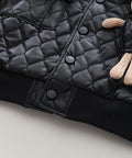 Black quilted jacket with a small plush toy on a light background