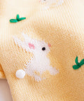 Yellow fabric with embroidered white rabbit and green leaves on a plain background