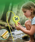 Child holding a yellow device with a screen, examining nature outdoors.