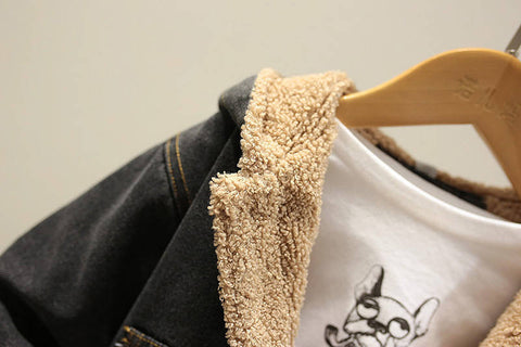 Close-up of a denim jacket with beige fleece lining on a hanger against a neutral background