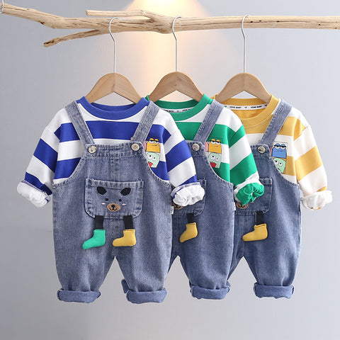 Three children's outfits with denim overalls and colorful shirts on hangers against a gray background.