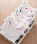 White baby shirts with cartoon designs on a wooden surface