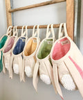 Set of colorful bunny slippers hanging on a wooden rack against a white wall.
