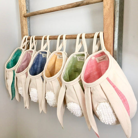 Set of colorful bunny slippers hanging on a wooden rack against a white wall.