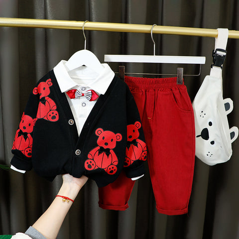 Children's outfit with black cardigan with red bear patterns, white shirt, red pants, and white bag on a rack.