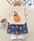 Children's outfit with pineapple-themed t-shirt and shorts on a hanger, accompanied by white sneakers.