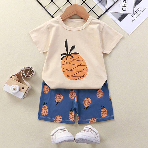 Children's outfit with pineapple-themed t-shirt and shorts on a hanger, accompanied by white sneakers.