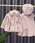 Pink children's coat and hat set on hangers against a gray curtain background