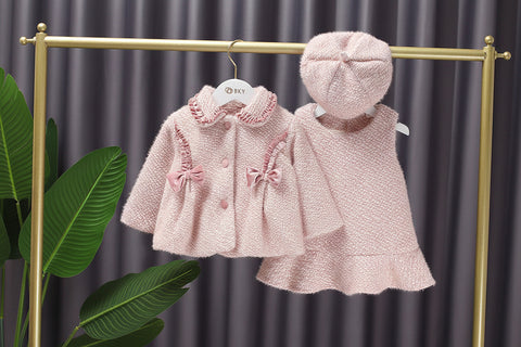 Pink children's coat and hat set on hangers against a gray curtain background