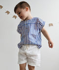 Child wearing a blue and white striped shirt and white shorts against a plain background