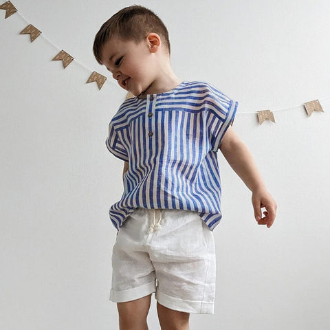 Child wearing a blue and white striped shirt and white shorts against a plain background
