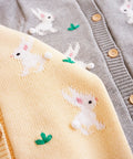 Close-up of a gray cardigan with embroidered white bunnies on a yellow fabric background.