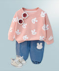 Children's outfit with pink sweater and blue jeans featuring bunny designs on a light blue background.