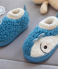 Blue plush slippers with a smiley face design held by a hand on a gray surface.