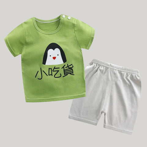 Children's green t-shirt with penguin design and white shorts on a white background