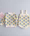 Children's floral-patterned cardigan and overalls on a beige surface with 'Love Lovely Ones' sign.
