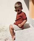 Child wearing sunglasses and a red shirt sitting on a concrete surface.