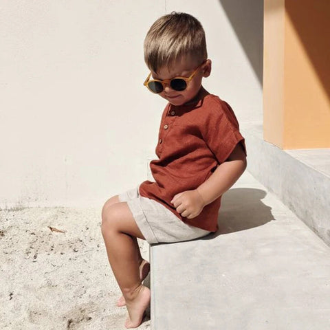 Child wearing sunglasses and a red shirt sitting on a concrete surface.
