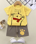 Children's yellow t-shirt with bear design and gray shorts on a beige surface.