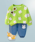 Green sweater with bunny patterns and blue pants on a light blue background