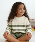 Young girl sitting on a chair wearing a striped sweater in a room with toys.