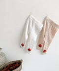 Two pairs of baby leggings with red accents on a white surface, next to a ceramic pot and bowl with berries.