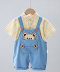 Children's outfit with blue overalls featuring bear design, yellow checkered shirt, and white pants on a hanger.