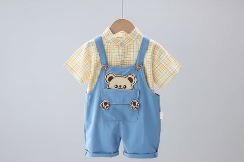 Children's outfit with blue overalls featuring bear design, yellow checkered shirt, and white pants on a hanger.