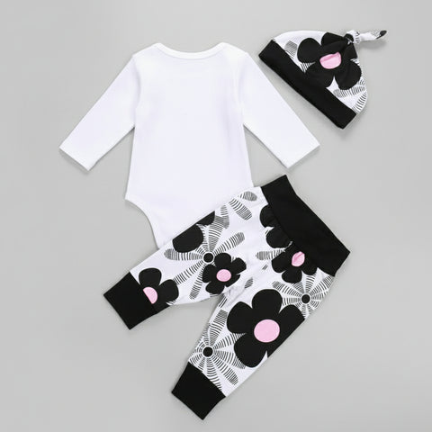 Baby outfit set with white long-sleeve top, black floral leggings, and matching hat on a wooden surface.