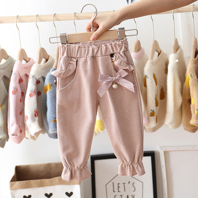 Pink baby pants with a bow on a hanger against a background of other children's clothes.