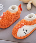 Orange and white baby shoe with a smiley face held by a hand on a gray surface.